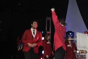 Two MMT students in red jacvkets, receive gold medals on stage. One student lifts arm in celebration