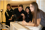 Three girls watch Taylor operate a camera