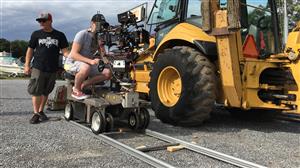 Ian sitting on a dolly and track with a Panavision camera, next to a Large yellow front-end-loader